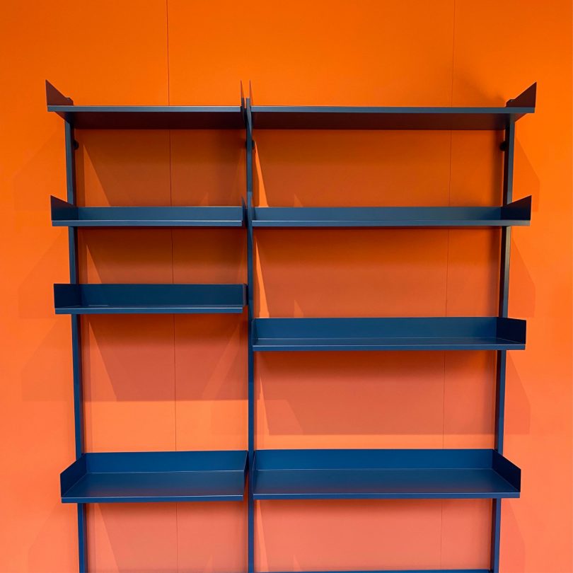 two modular metal shelves with adjustable components on bright orange wall