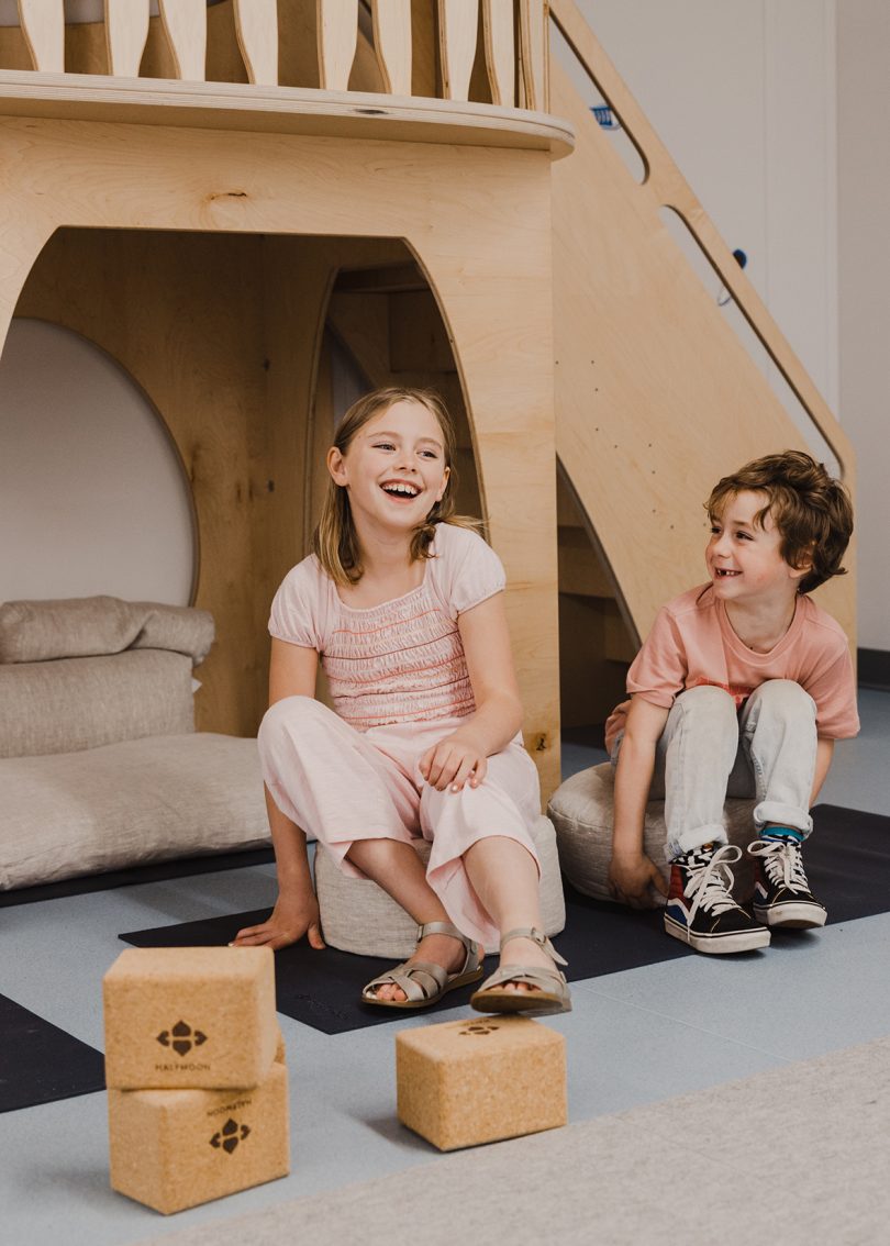 two light-skinned children sitting on a yoga mat laughing