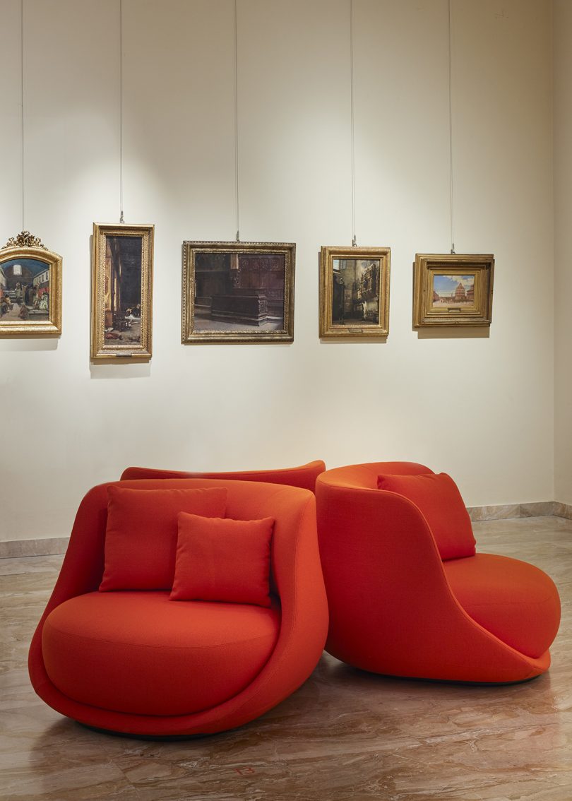 three chunky vermillion chairs in a gallery-like space with traditional wall art