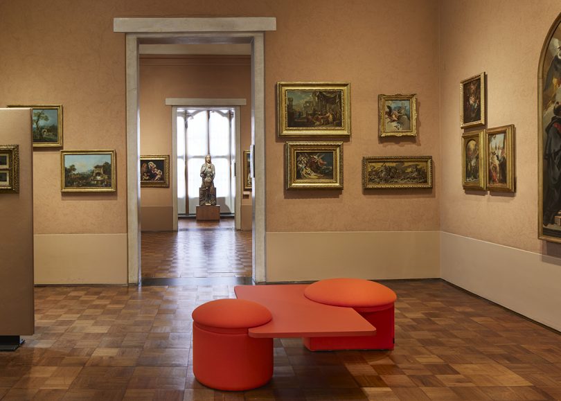 vermillion red seating/table combo in gallery-like space with traditional wall art