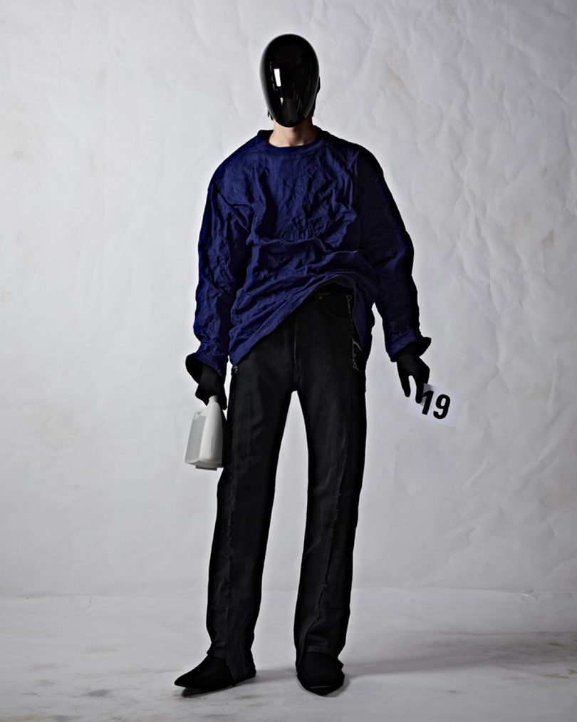 Balenciaga couture model in blue sweater with full black face mask holding white Bang & Olufsen Speaker Bag.