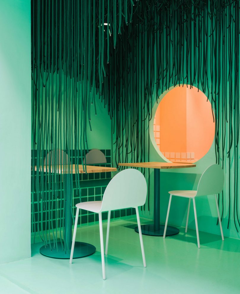modern restaurant interior with green tones and circular window looking through to peach room