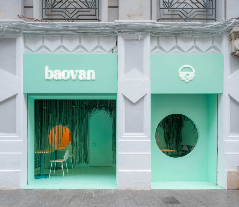 restaurant exterior shot of building with white and pale green paint with large circular window looking inside