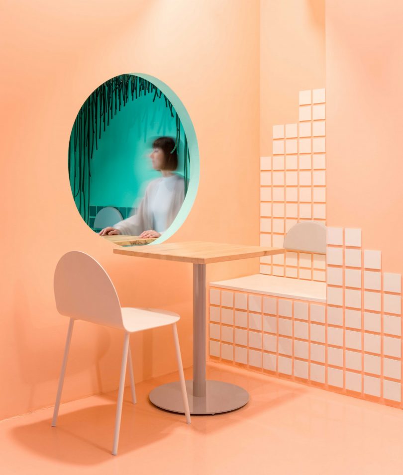 modern restaurant interior with peach colored walls with a white square pattern and green hued window with woman sitting on the other side