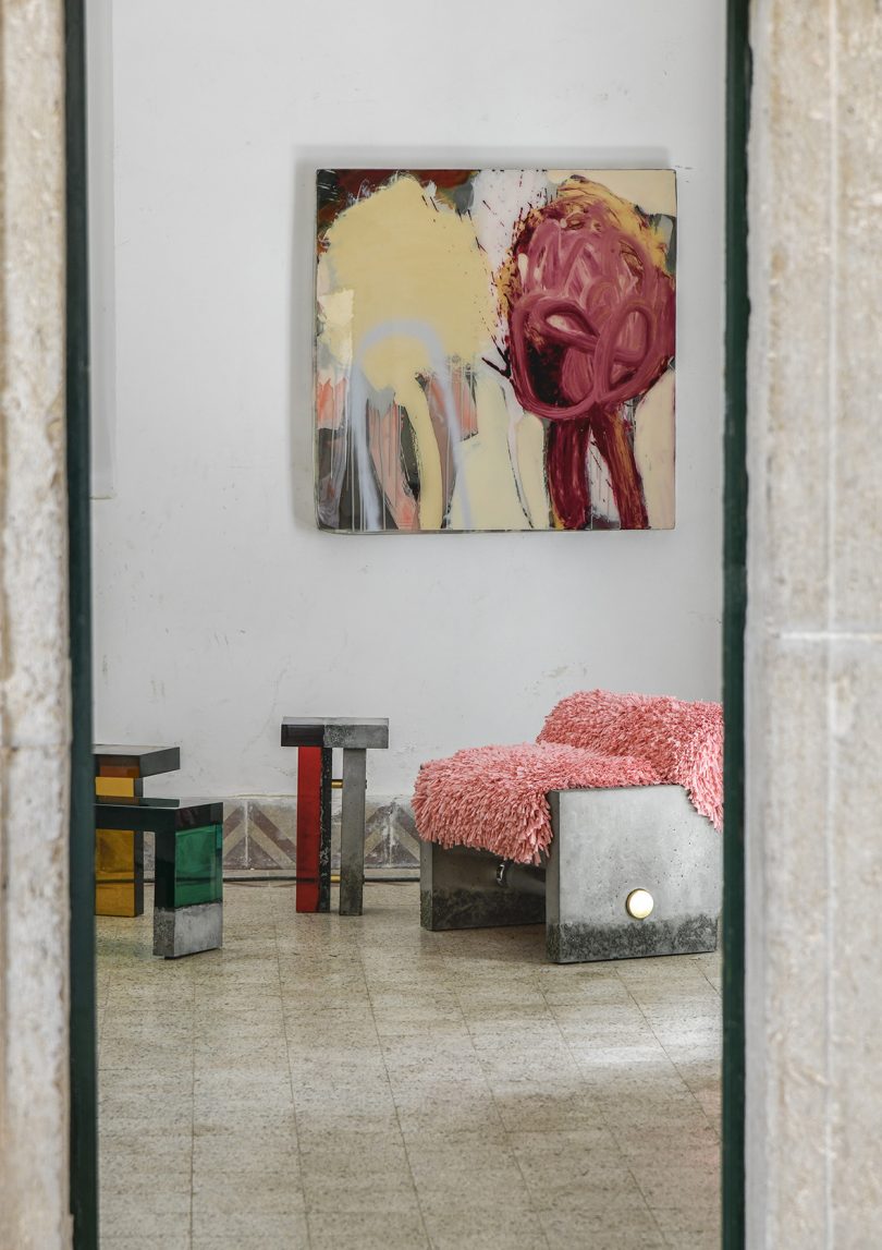 three concrete and resin table, an armchair, and large piece of wall art in an interior space