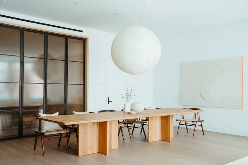 long light wood table with dining chairs and a large white orb of lighting suspended above it