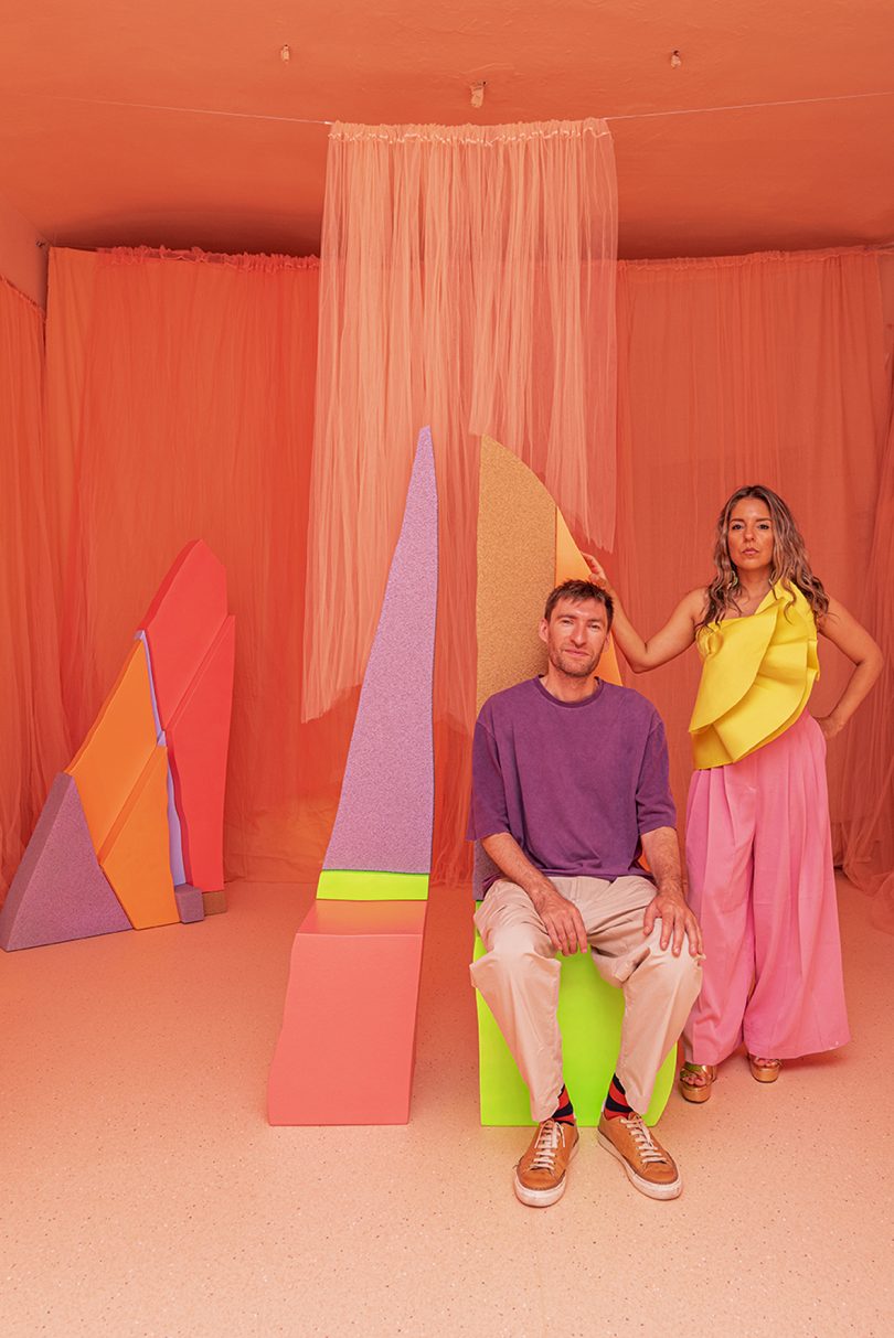 two people standing and sitting in the middle of an exhibition of neon colored forms