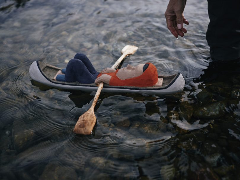 small wooden toy boat with man lying with knees up with small oars in hand