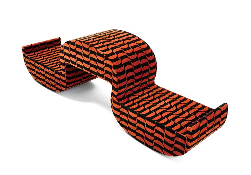 piece of furniture shaped like a parentheses and covered in matching patterned fabric on white background