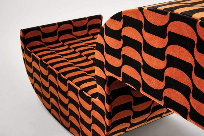 detail of piece of furniture shaped like a parentheses and covered in matching patterned fabric on white background