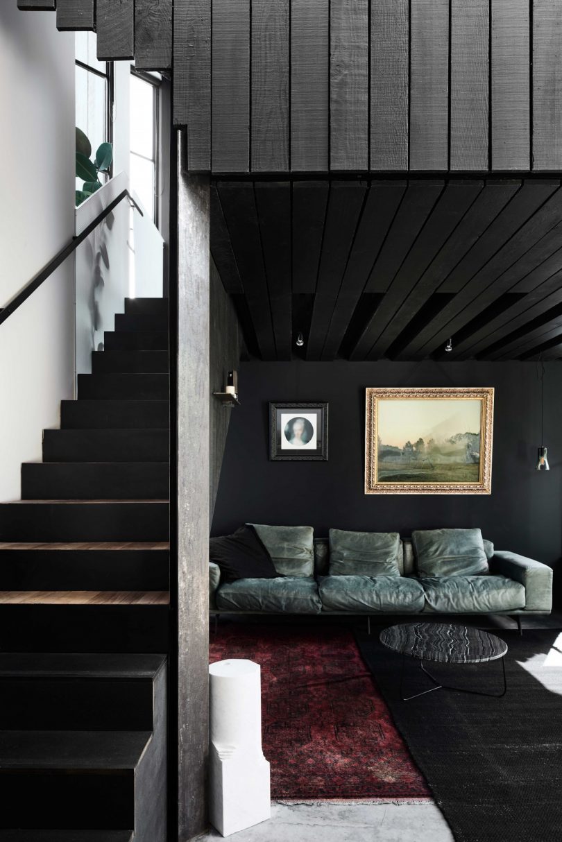interior of modern home with view of dark living room with green sofa and black staircase