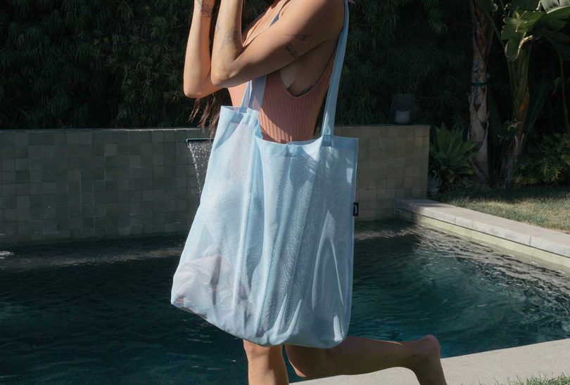 Outdoor shot of cropped person holding light blue tote bag in front of pool