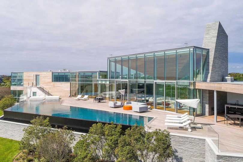 Back exterior view of mansion in Hamptons with glass exterior walls and massive pool