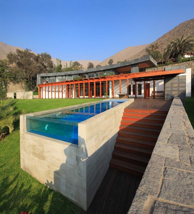 backyard view of an elongated concrete pool that juts out from the earth with a glass panel at the end