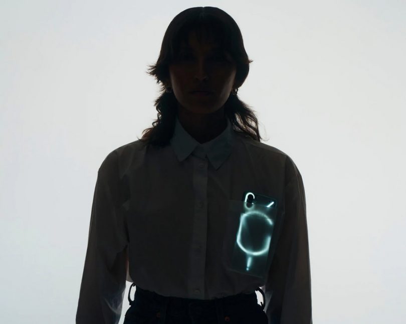 Nothing Phone 1 glowing through the front pocket of woman wearing a white button up shirt.