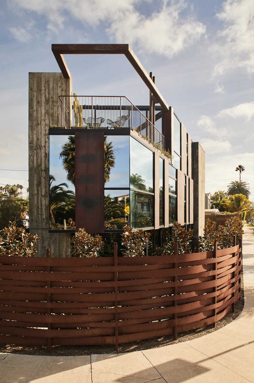 closeup exterior view of modern, industrial house with mirrored windows and rust red fence
