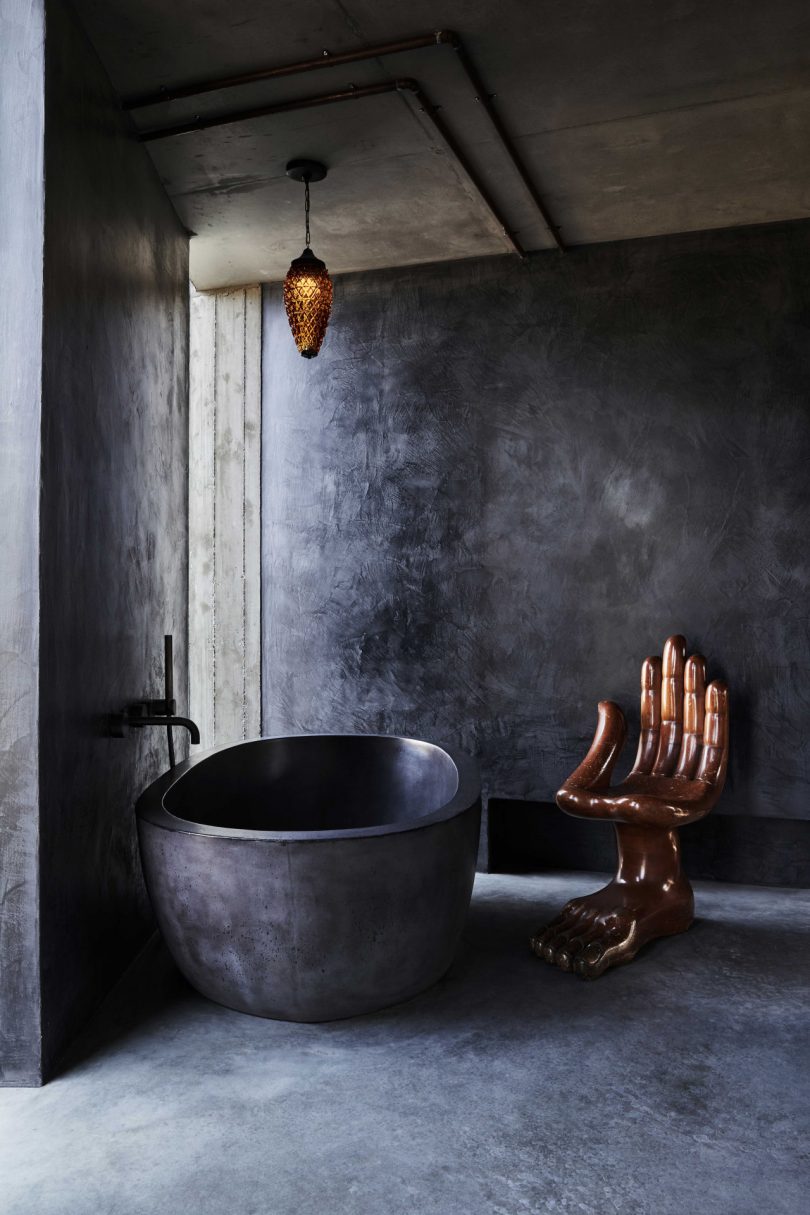 modern interior of dark minimalist bathroom with polished concrete surfaces and oval bathtub