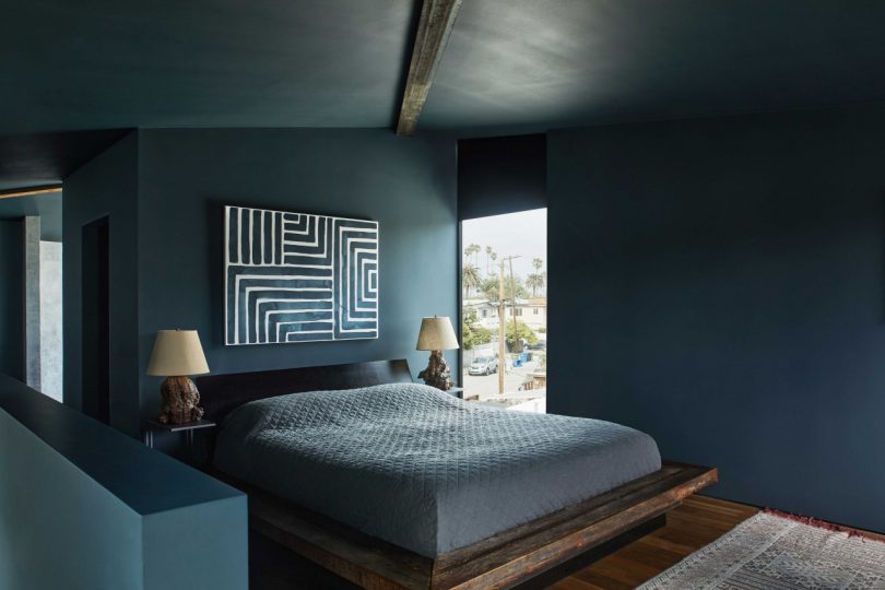 interior modern bedroom with deep blue walls and bedding with graphic painting over bed