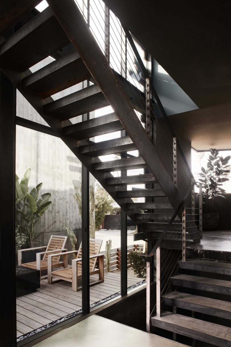 interior view of open metal staircase in front of large windows looking out to deck