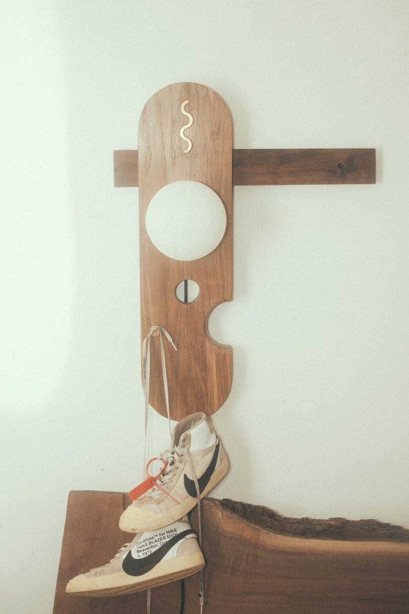 abstract lamp with wood hanging on a white wall with a pair of Nikes hanging from it
