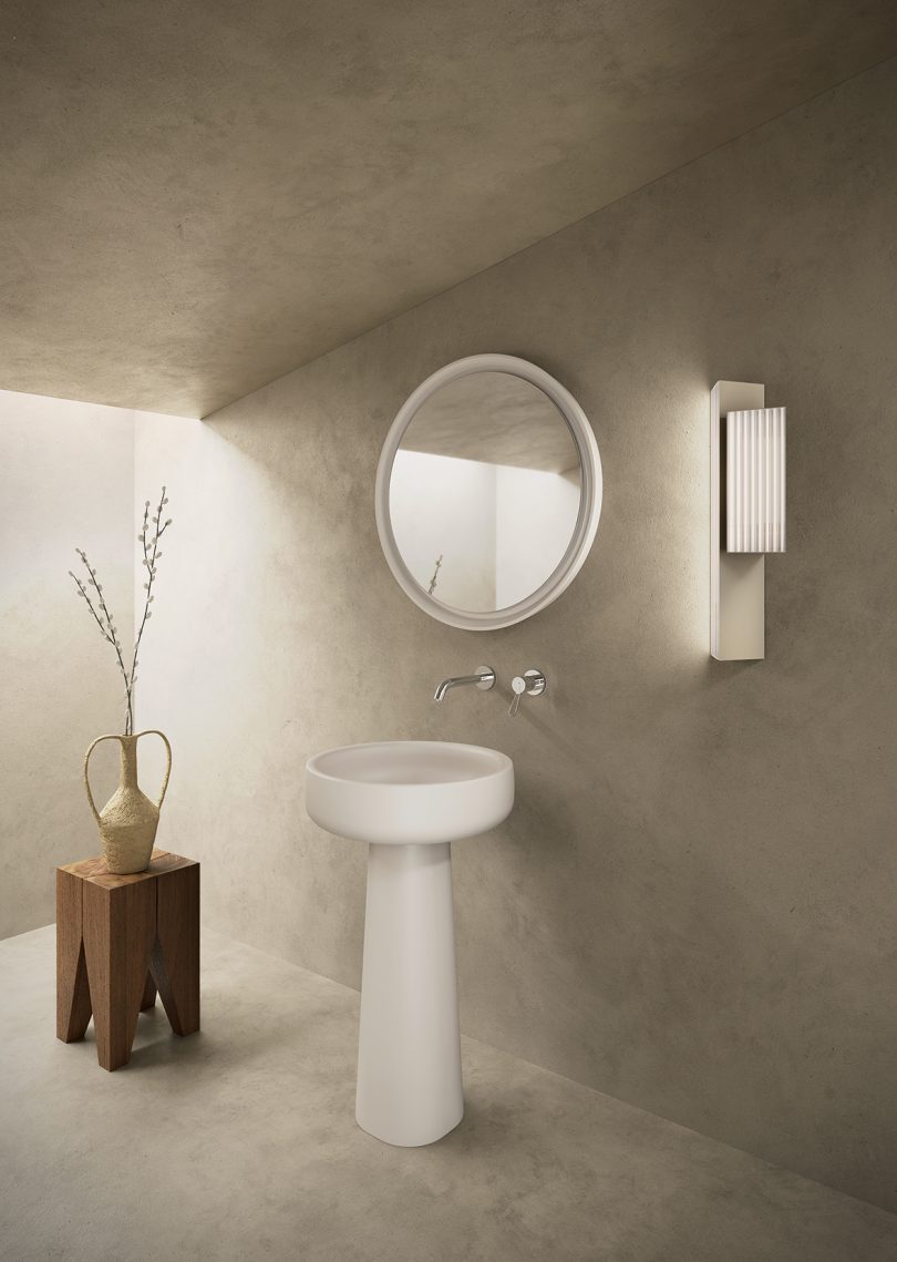 bathroom with round pedestal sink, small wood side table, round mirror, and rectangular wall sconce