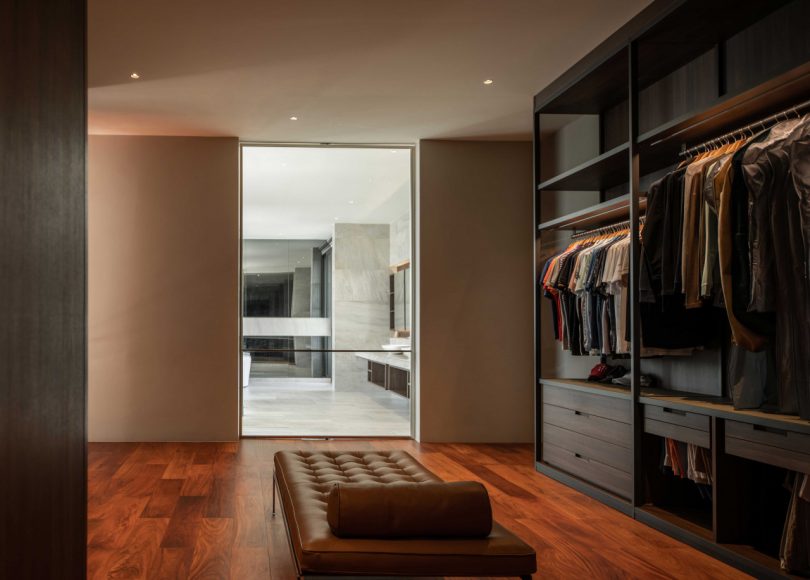 interior shot of large modern closet and dressing area with wood accents looking into bathroom