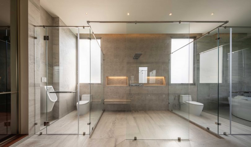 large bathroom sectioned off in glass with neutral tone tiles