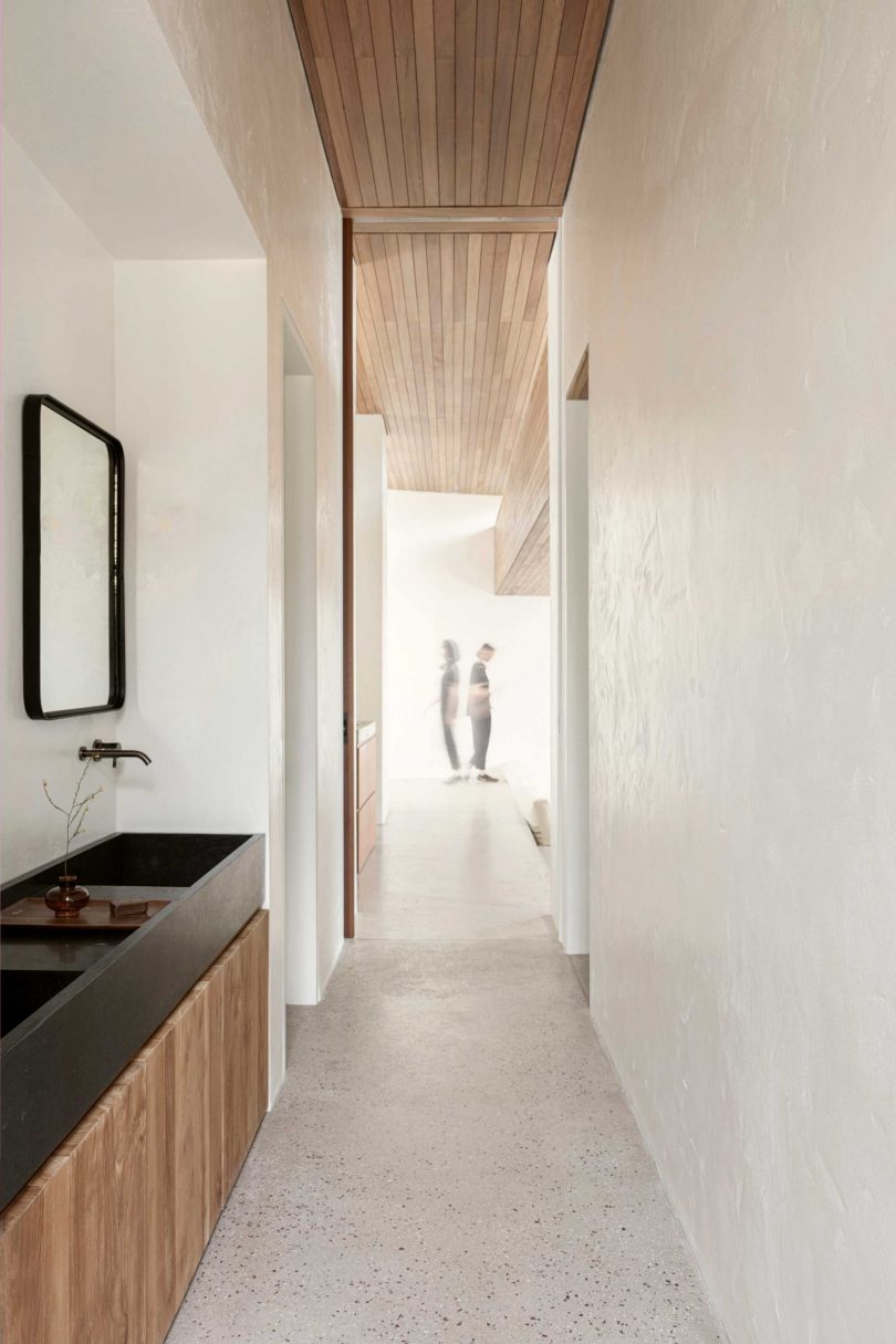 long hallway view with light at the end and minimalist black and wood sinks on side wall