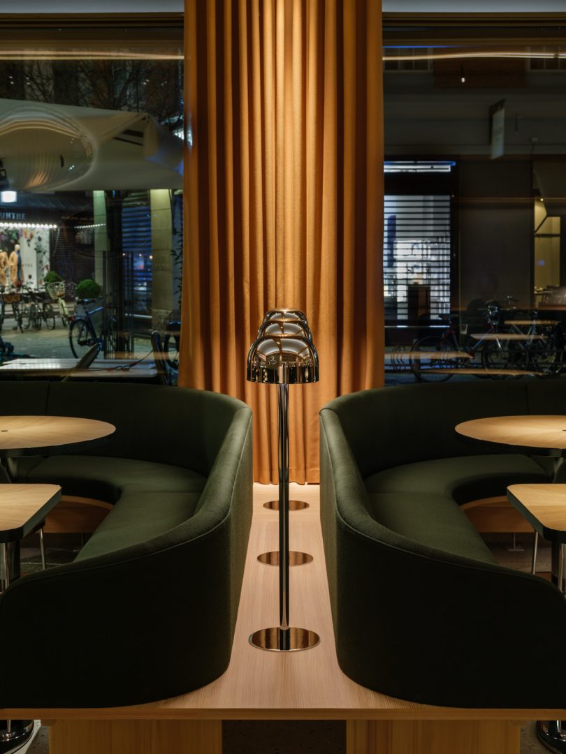 restaurant interior looking between two dark green booth tables with series of lamps
