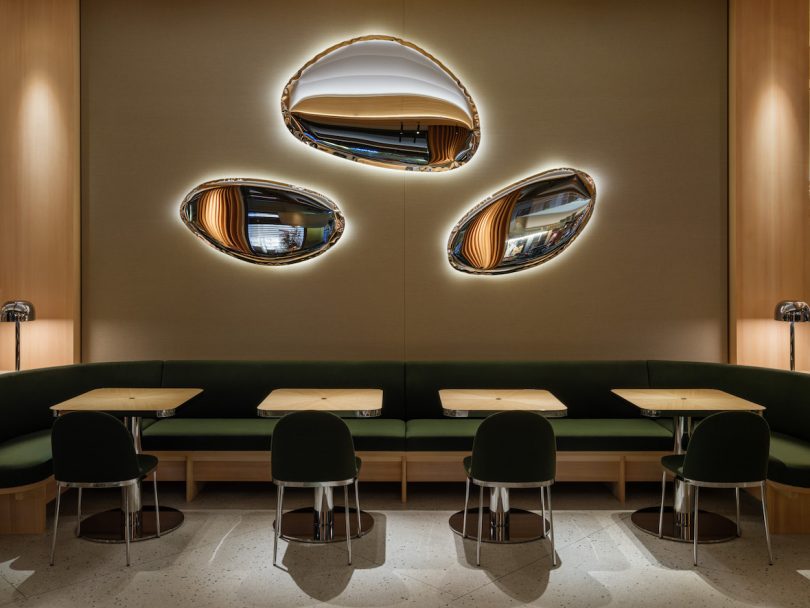 restaurant interior with four tables with dark green seating and puffed metal mirrors above