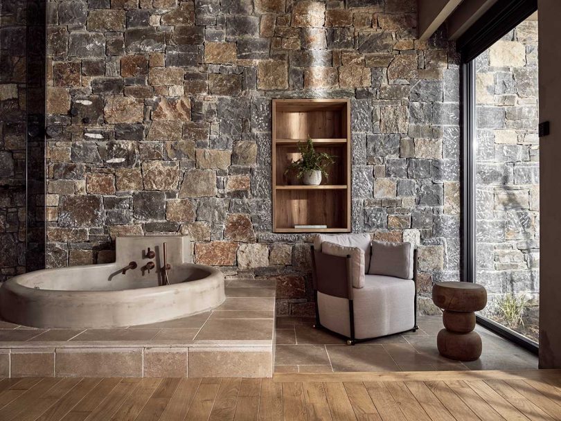 interior view of modern hotel room in neutral furnishings with rocky wall and round in-ground tub