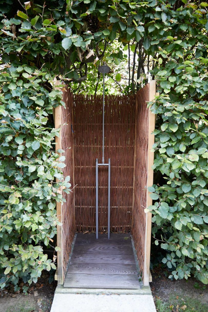 exterior view of outdoor shower clad in wood panels embedded in lush greenery