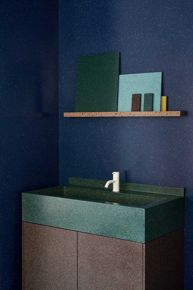 closeup of showroom vignette featuring dark blue walls with dark green sink and shelves holding surface material samples