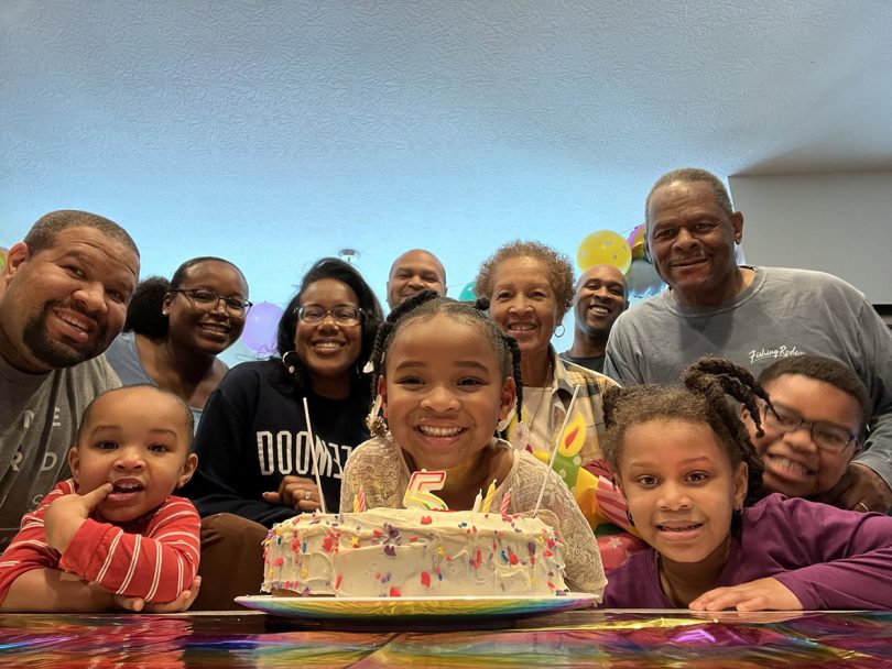 family photo with everyone standing behind a birthday cake