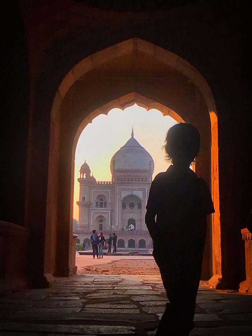 child standing in an archway looking at a building in India