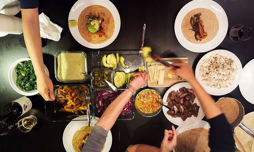 overhead photo of a table full of food with arms reaching for different dishes