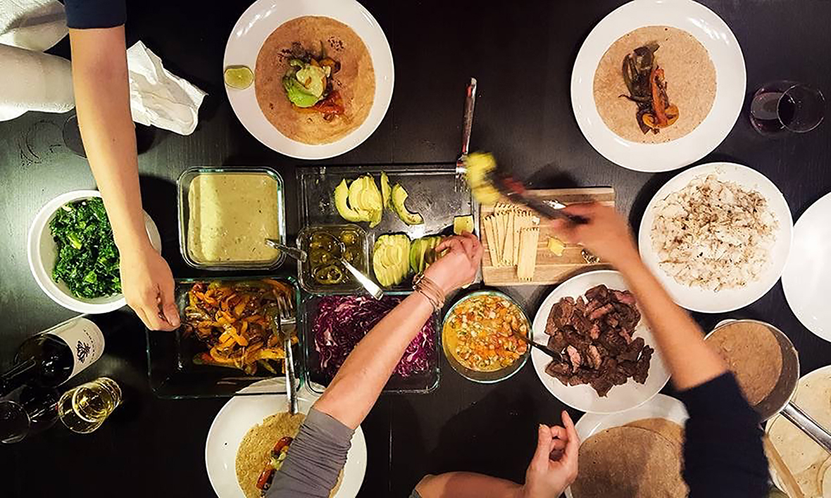 overhead photo of a table full of food with arms reaching for different dishes