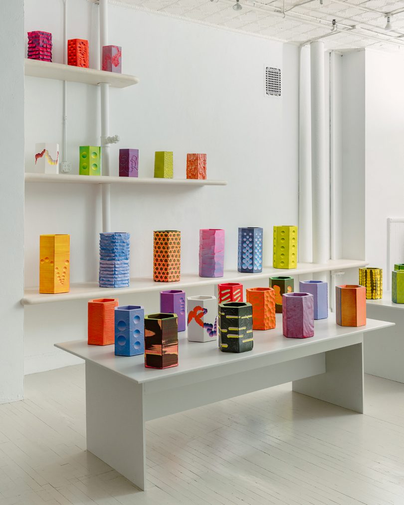 white gallery space with shelves and a table full of bright colorful vessels
