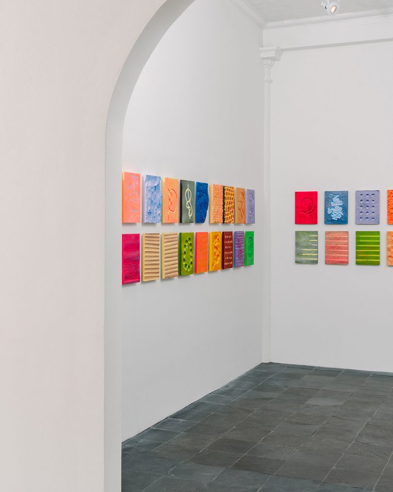 white gallery space with hung with small, colorful rectangular-shaped works of art