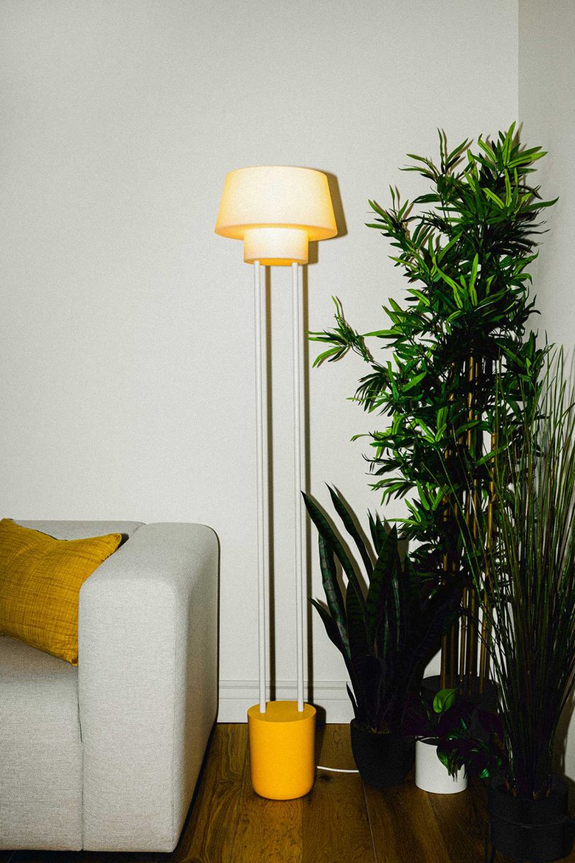 slim floor lamp between a neutral sofa and tall plant