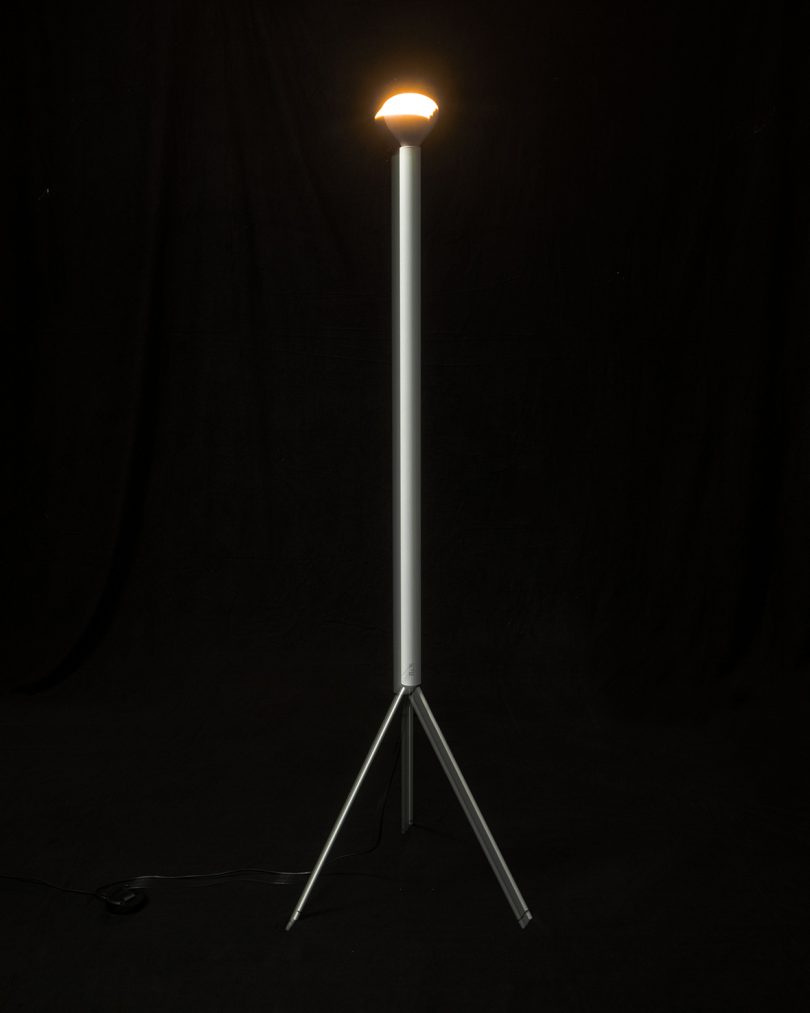 white slim tripod floor lamp lit up with a black background