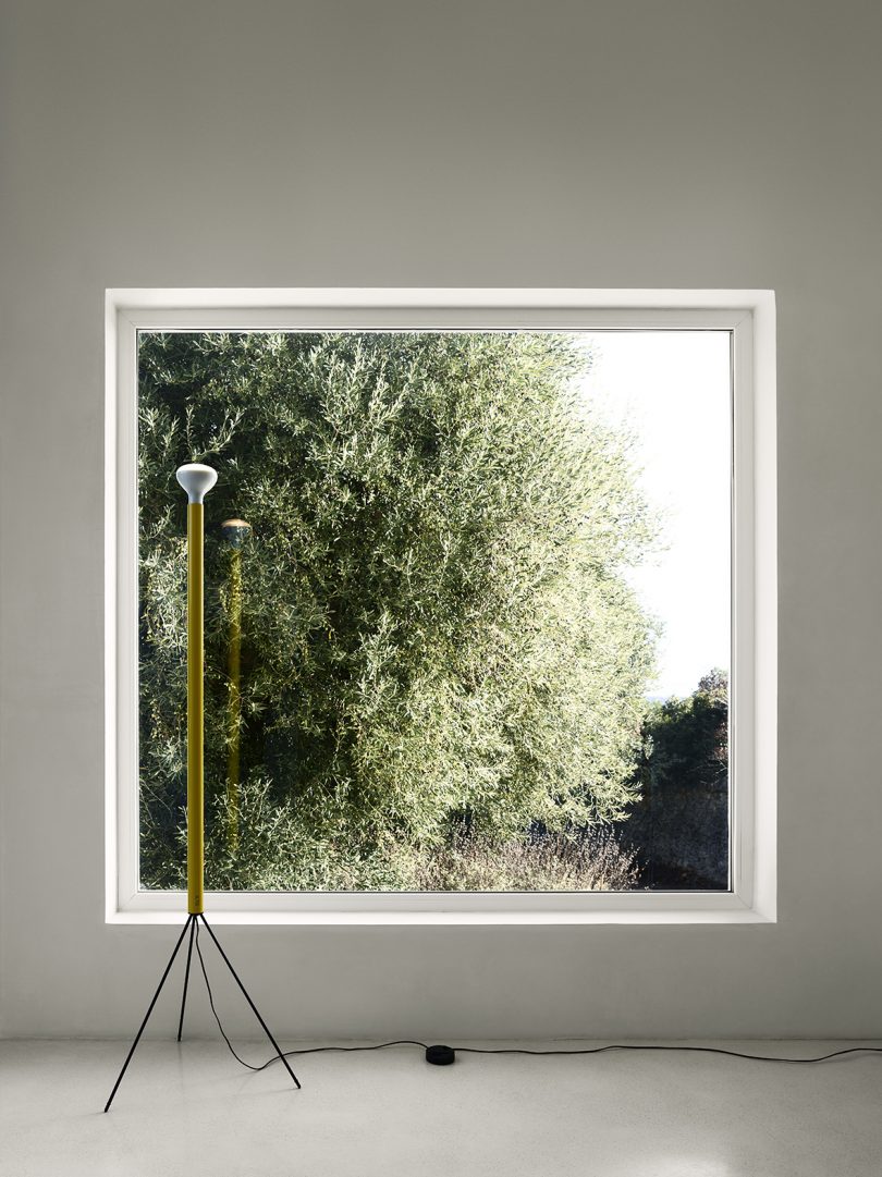 yellow slim tripod floor lamp in front of large square window looking out on trees