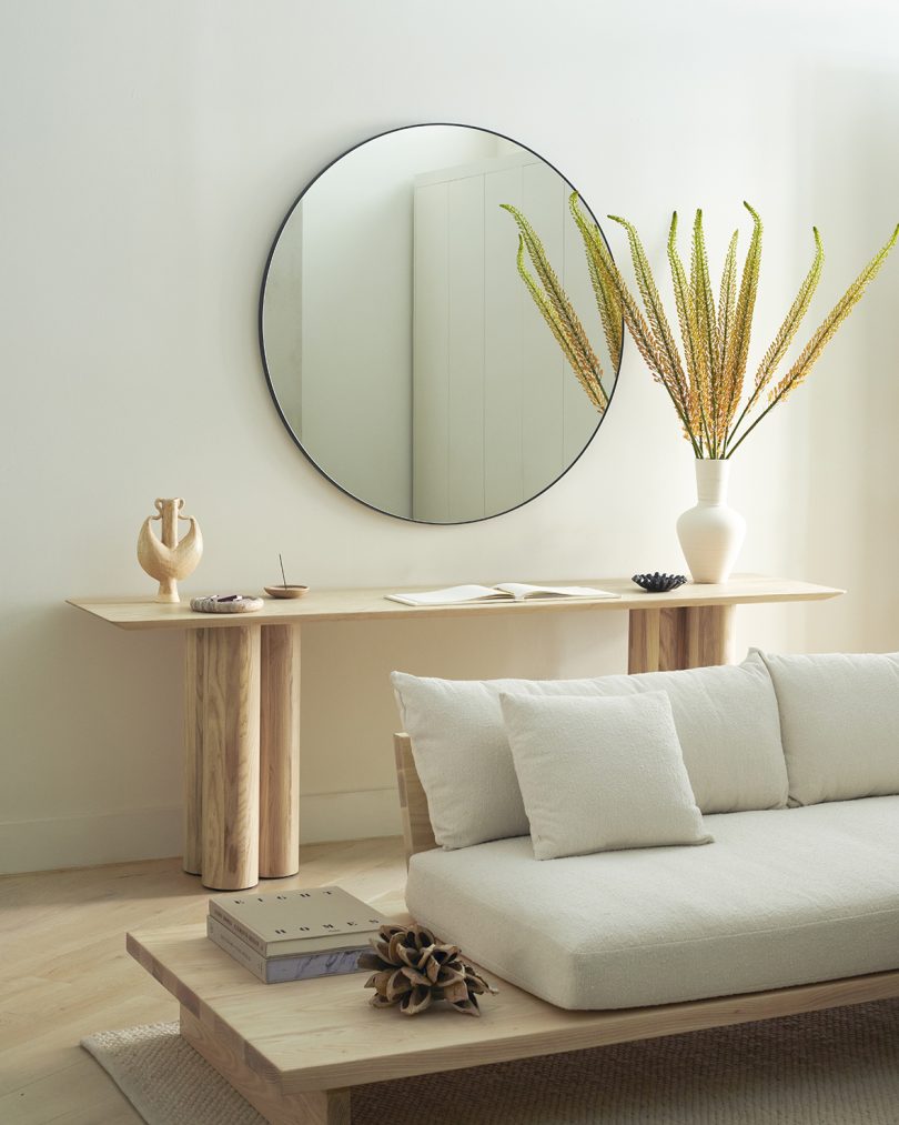 styled interior space with white sofa, side table, console table, and large round mirror