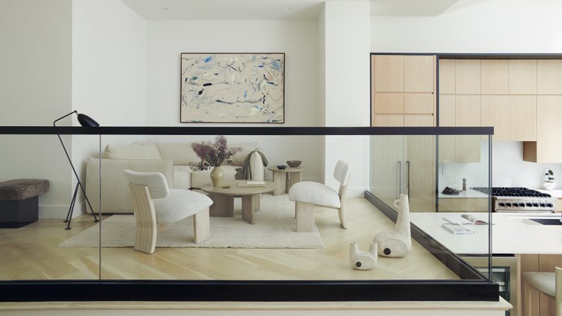 styled interior space with white upholstered chairs, a coffee table, art, and a clear glass partition