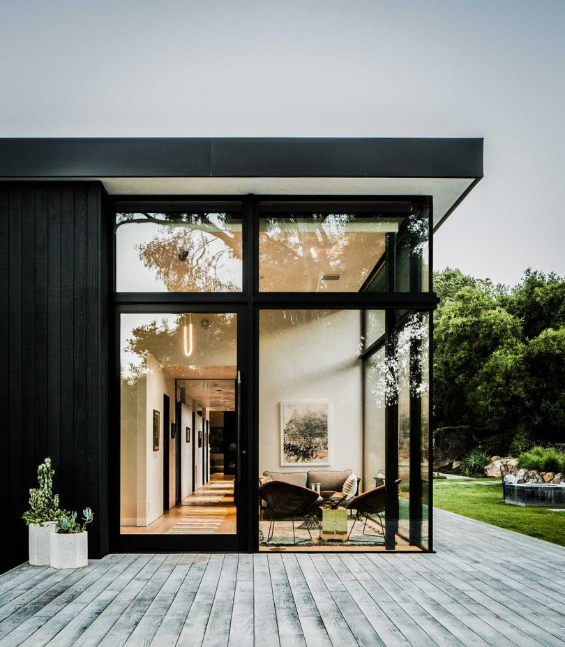 exterior end view of modern box-like home with black exterior and window walls