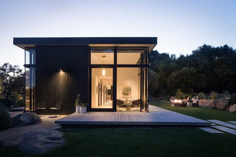 exterior twilight view of modern box-like home with black exterior and window walls