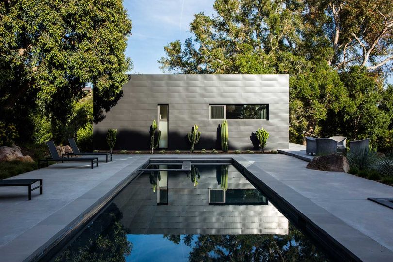 exterior view of modern box-like home with black exterior and long pool