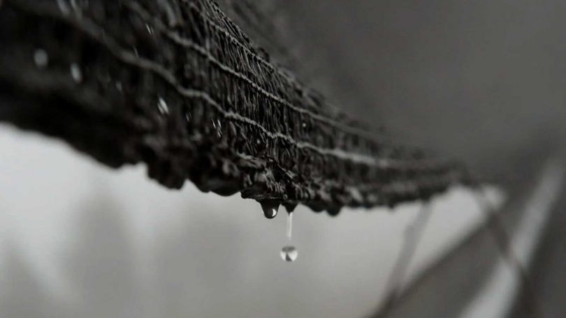 bottom of black fabric mesh with droplet of water about to fall