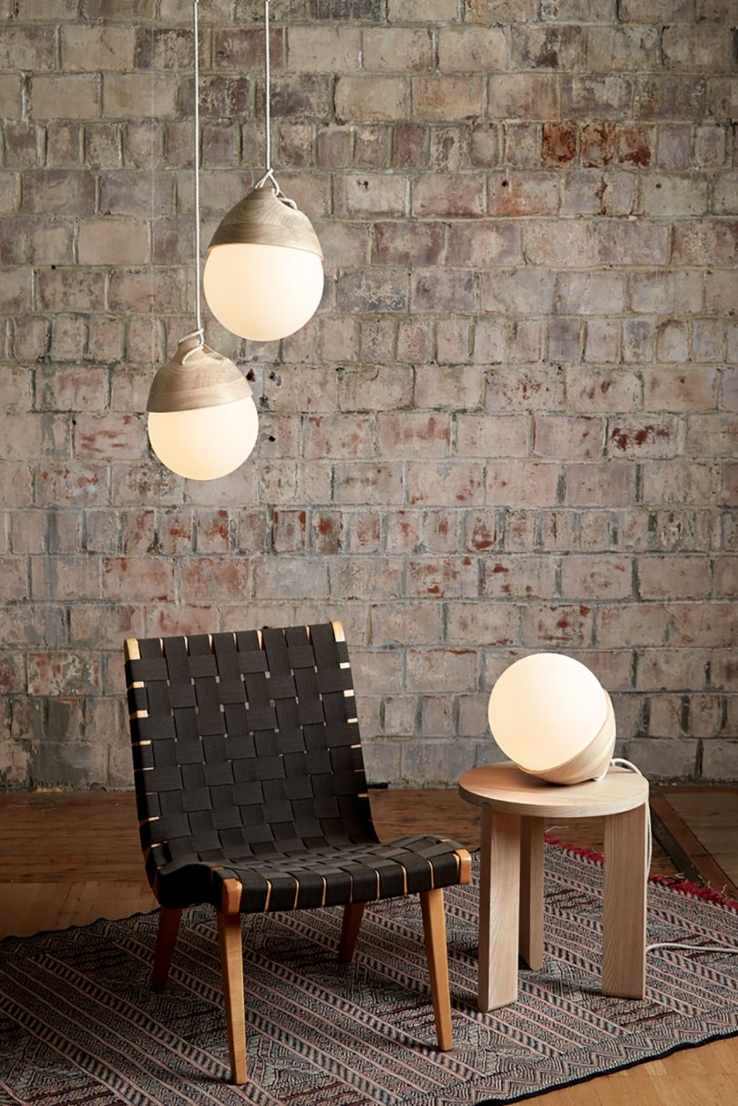 Two hanging Booi lights and one placed on small side table staged in room with brick wall.