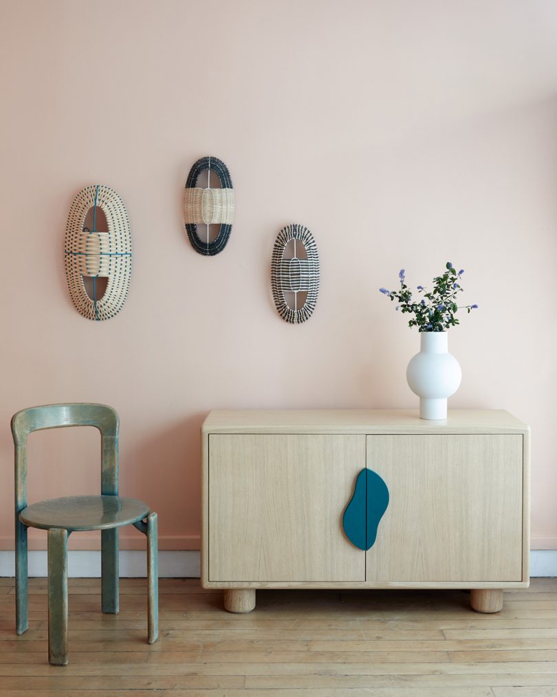 light wood sideboard in a styled space with dining chair, 3D wall art, and a vase of flowers